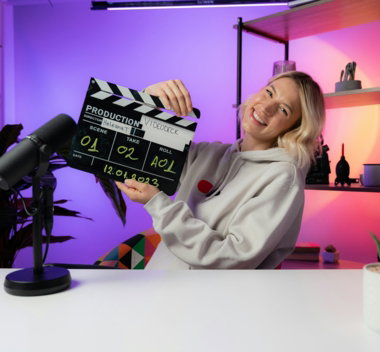 a woman sitting at a table holding a movie clapper